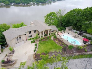 A two-story house with a swimming pool, a well-maintained lawn, and a view of a lake.
