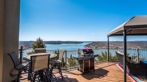 A deck with a grill, wicker chairs, and a table overlooking a lake. - Bella Lago House (Osage Beach)