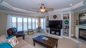 A spacious living room with a large window, leather sofa, wooden coffee table, and a fireplace. - Bella Lago House (Osage Beach)