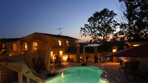 A swimming pool with a slide, a covered patio area, and a house with multiple windows and a chimney. - Bella Lago House (Osage Beach)