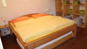 Ein hölzernes Bett mit zwei Kissen, ein Nachttisch mit Lampe und ein Regal mit Aufbewahrungsboxen.