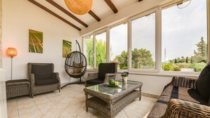 A sunlit room with wicker furniture, large windows, and a hanging chair. - Villa Tanga near Rovinj with Pool (Rovinj)