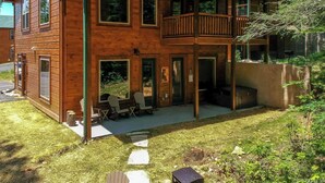 Una cabaña de madera de dos pisos con balcón, mobiliario exterior y entorno natural.