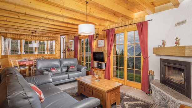 A cozy cabin interior with a wooden ceiling, a fireplace, a sofa, a coffee table, and a TV.