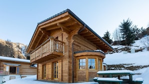A wooden cabin with a balcony, large windows, and a snow-covered ground.