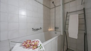 A bathroom with white tiles, a shower, a towel rack, and a small decorative item on the sink.