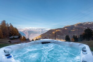 A hot tub with a view of mountains and a house in the background.