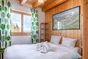 A bedroom with a bed, white bedding, a wooden headboard, a window with curtains, and a painting on the wall.