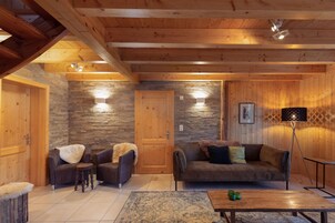 A cozy wooden interior with a stone wall, two sofas, a coffee table, and a lamp.