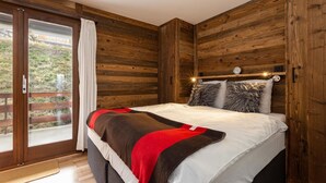 A bedroom with a large bed, wooden walls, a sliding glass door, and a small shelf with decorative items. - App Les Rocailles 9 Family Retreat With Sauna (Riddes)
