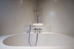 Bathroom features a large oval-shaped bathtub with a handheld showerhead and a shelf for towels.