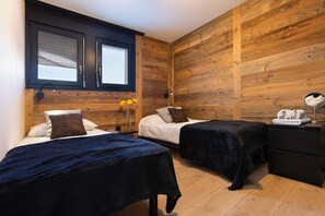 Cozy bedroom with two single beds, a wooden panel wall, and a bedside table with a lamp and mirror.