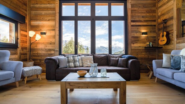 A cozy log cabin interior with a large window, a wooden coffee table, and two sofas. - Chalet Lupin (Riddes)