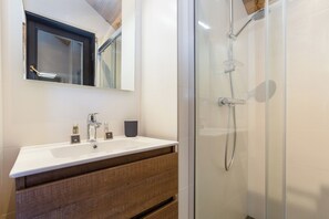 Bathroom features a glass-enclosed shower with handheld showerhead and wall-mounted controls.
