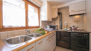 Una cocina con un lavamanos de acero inoxidable, armarios de madera, un microondas, una estufa y una ventana con cortinas de encaje.