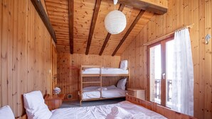 Una habitación de cabaña de madera con literas, una lámpara colgante, una ventana con cortinas y una mesita de noche pequeña.