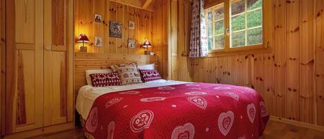 Een slaapkamer met houten lambrisering, een bed, twee wandlampen en een raam met uitzicht op groen.