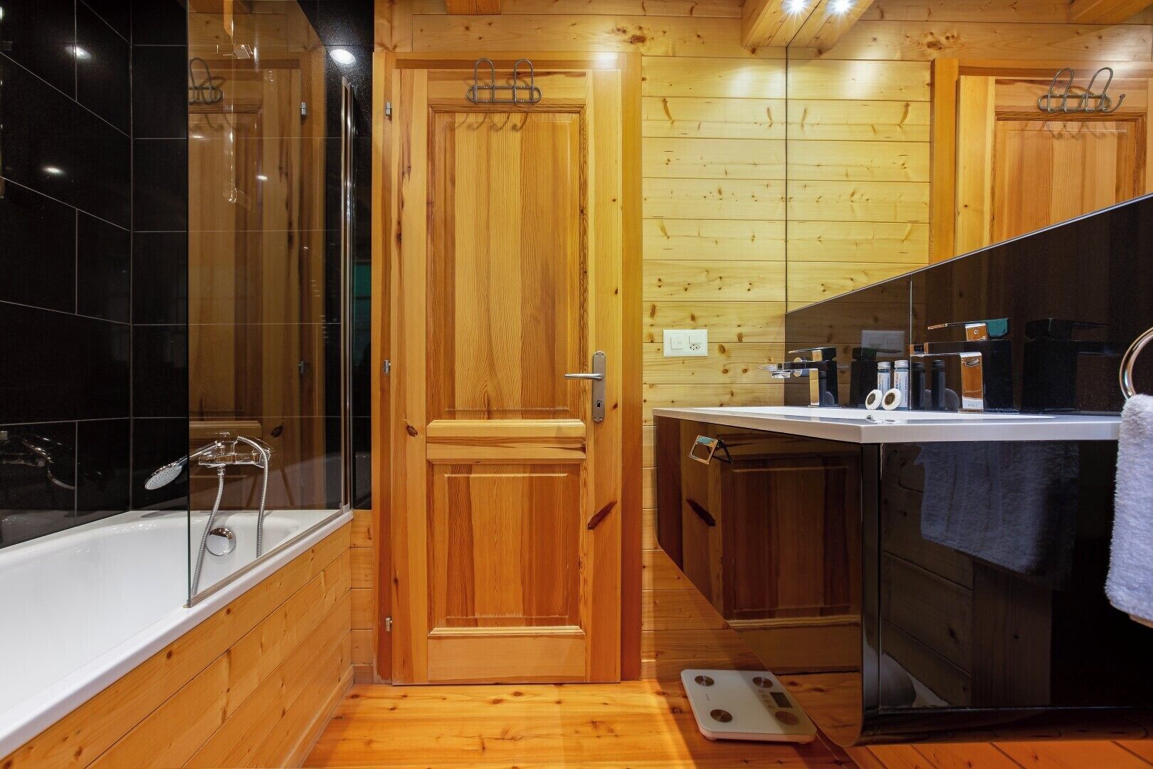 Een houten badkamer met een bad, een douche en een wastafel met een spiegel.
