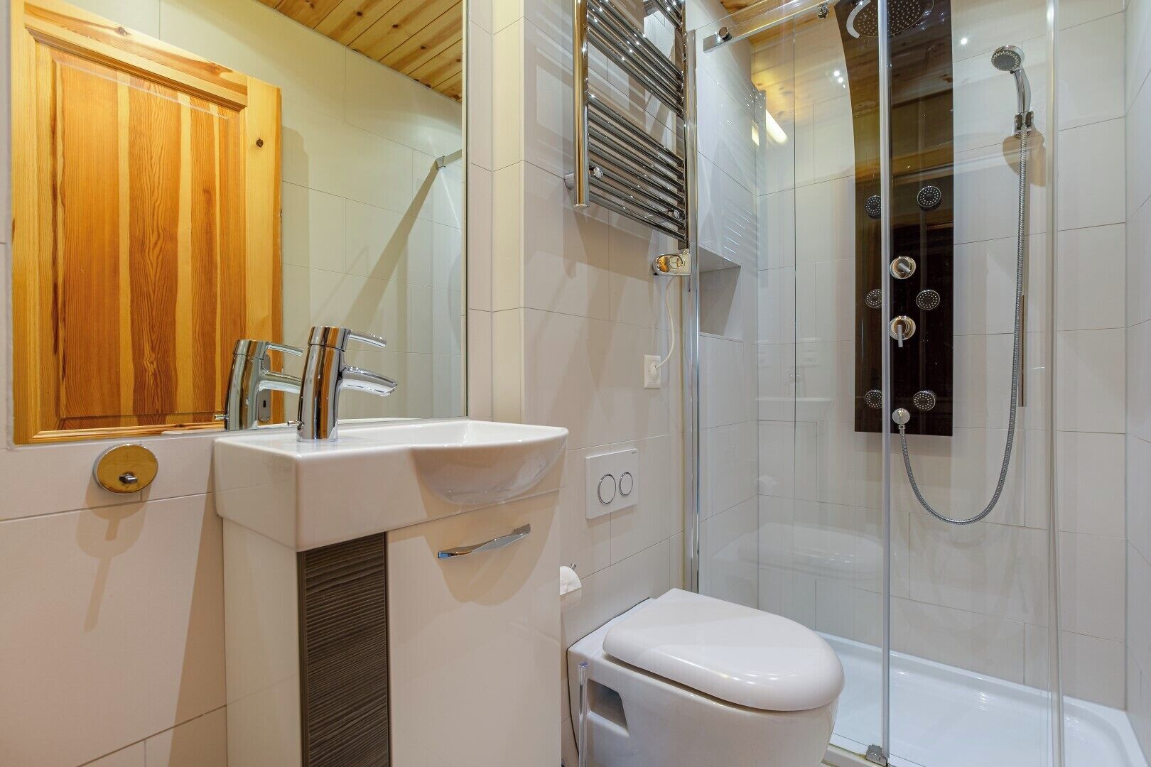 Ein modernes Badezimmer mit einem Holzkosmetikschrank, einer weißen Toilette, einer Duschkabine mit mehreren Brauseköpfen und einem Spiegel über dem Waschbecken.