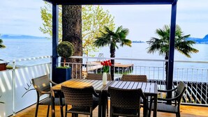 Een balkon met rieten meubilair, een houten tafel en uitzicht op het water.