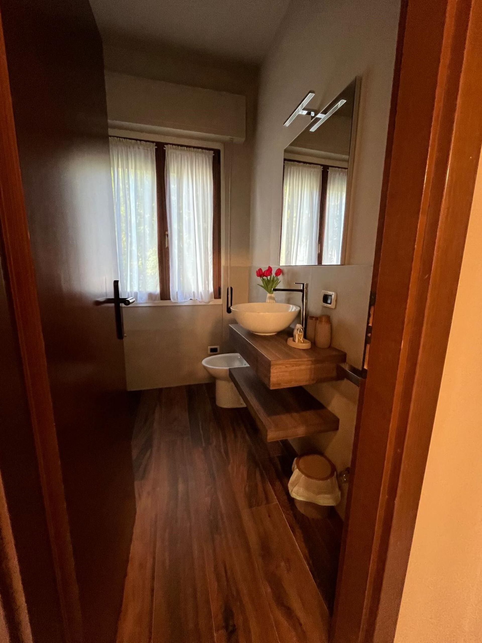 Een smalle badkamer met een houten vloer, een witte wastafel en een spiegel erboven.
