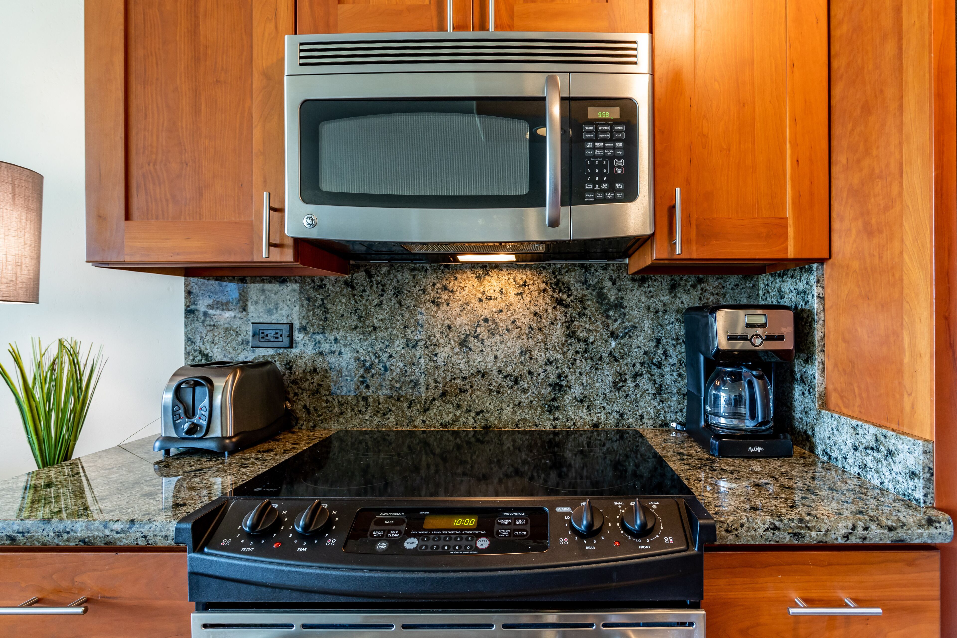 A kitchen with a stainless steel microwave, a toaster, and a coffee maker on a granite countertop.