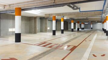 A parking garage with concrete pillars, directional arrows on the floor, and overhead pipes.