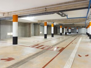 A parking garage with concrete pillars, directional arrows on the floor, and overhead pipes. - ibis budget Épinal (Epinal)