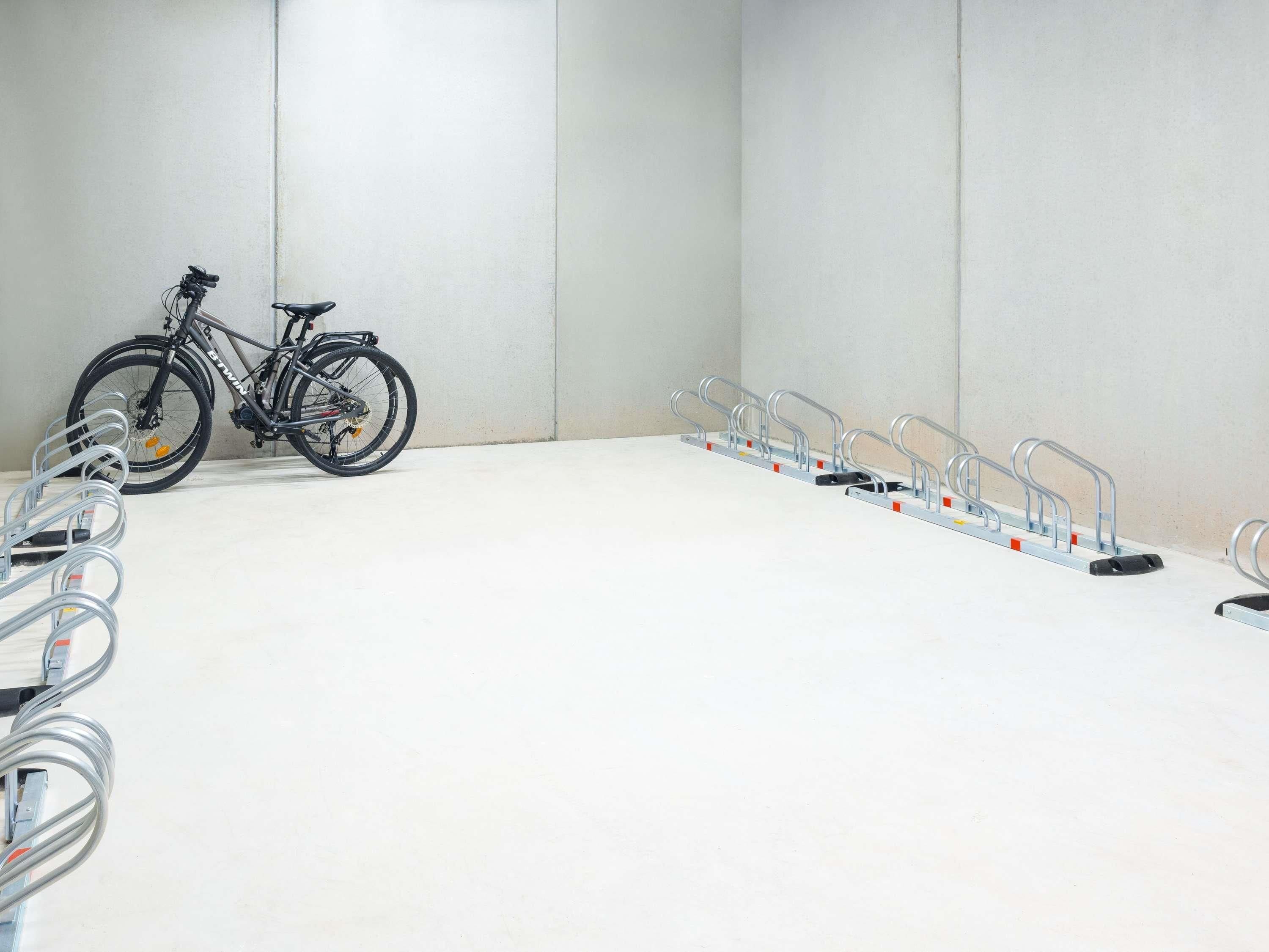 Ein Fahrrad steht neben einer Reihe von Fahrradständern in einem Raum mit schlichten Wänden und einem weißen Boden.