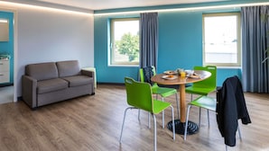 A modern room with a sofa, a dining table with chairs, and large windows.