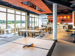 A modern dining area with tables and chairs, a ping pong table, and a kitchen area with a counter and appliances.