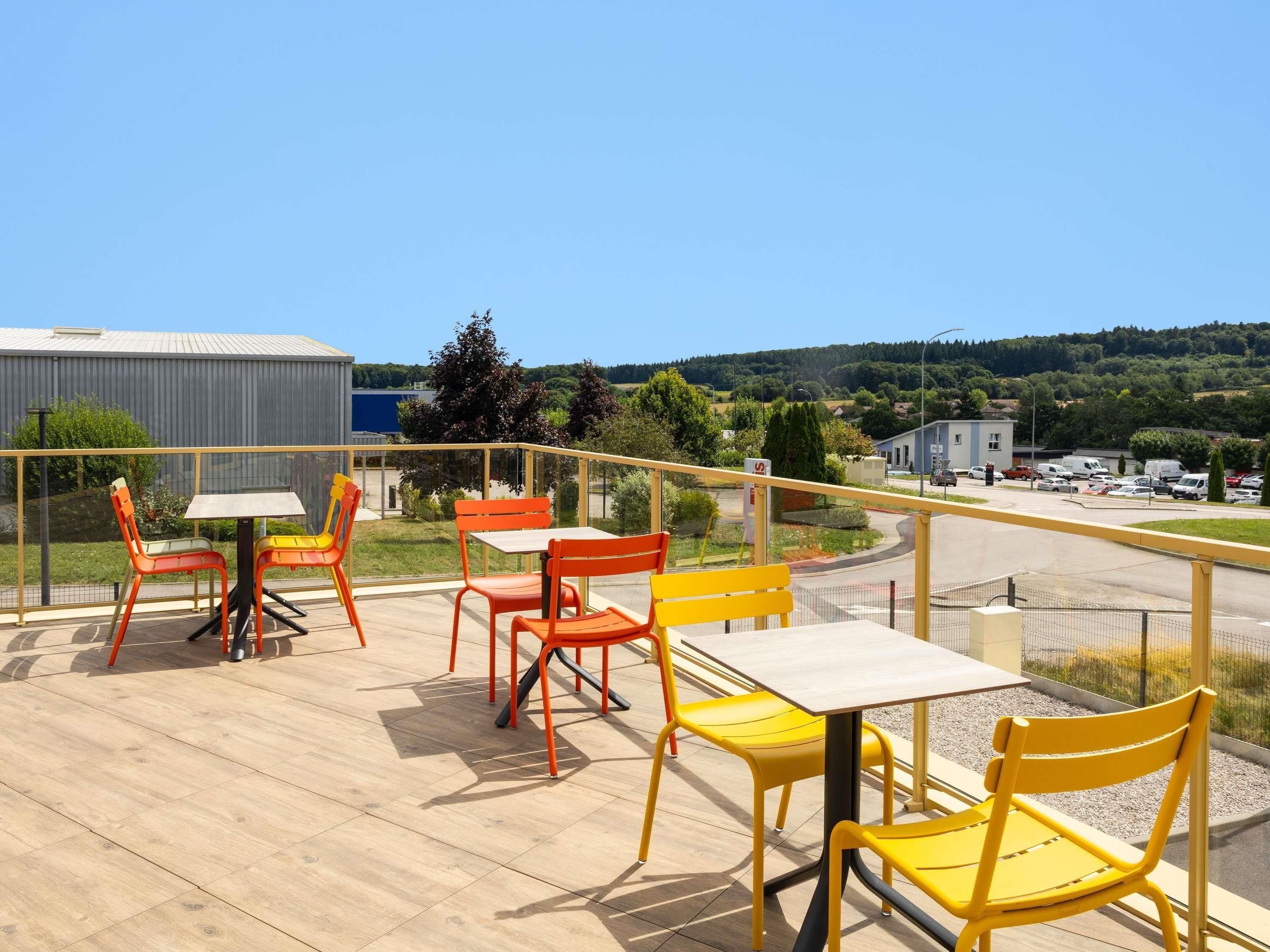 A terrace with outdoor seating and a view of a parking area and buildings.