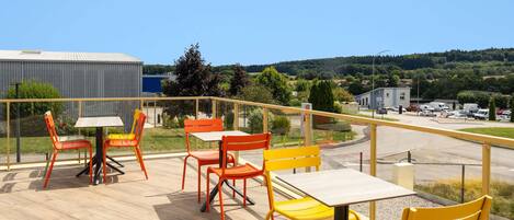 A terrace with outdoor seating and a view of a parking area and buildings.