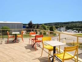 A terrace with outdoor seating and a view of a parking area and buildings.