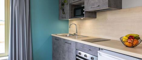 A modern kitchen with grey cabinets, a stainless steel sink, an oven, and a microwave.