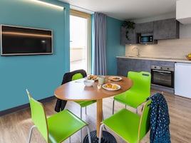 Una cocina moderna con microondas, horno y lavabo. Hay una mesa de comedor con sillas y un televisor montado en la pared.