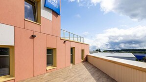 A modern building with a 'ibis budget' sign, large windows, and a flat roof with a railing.