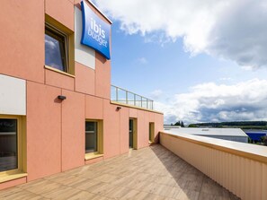 A modern building with a 'ibis budget' sign, large windows, and a flat roof with a railing. - ibis budget Épinal (Epinal)