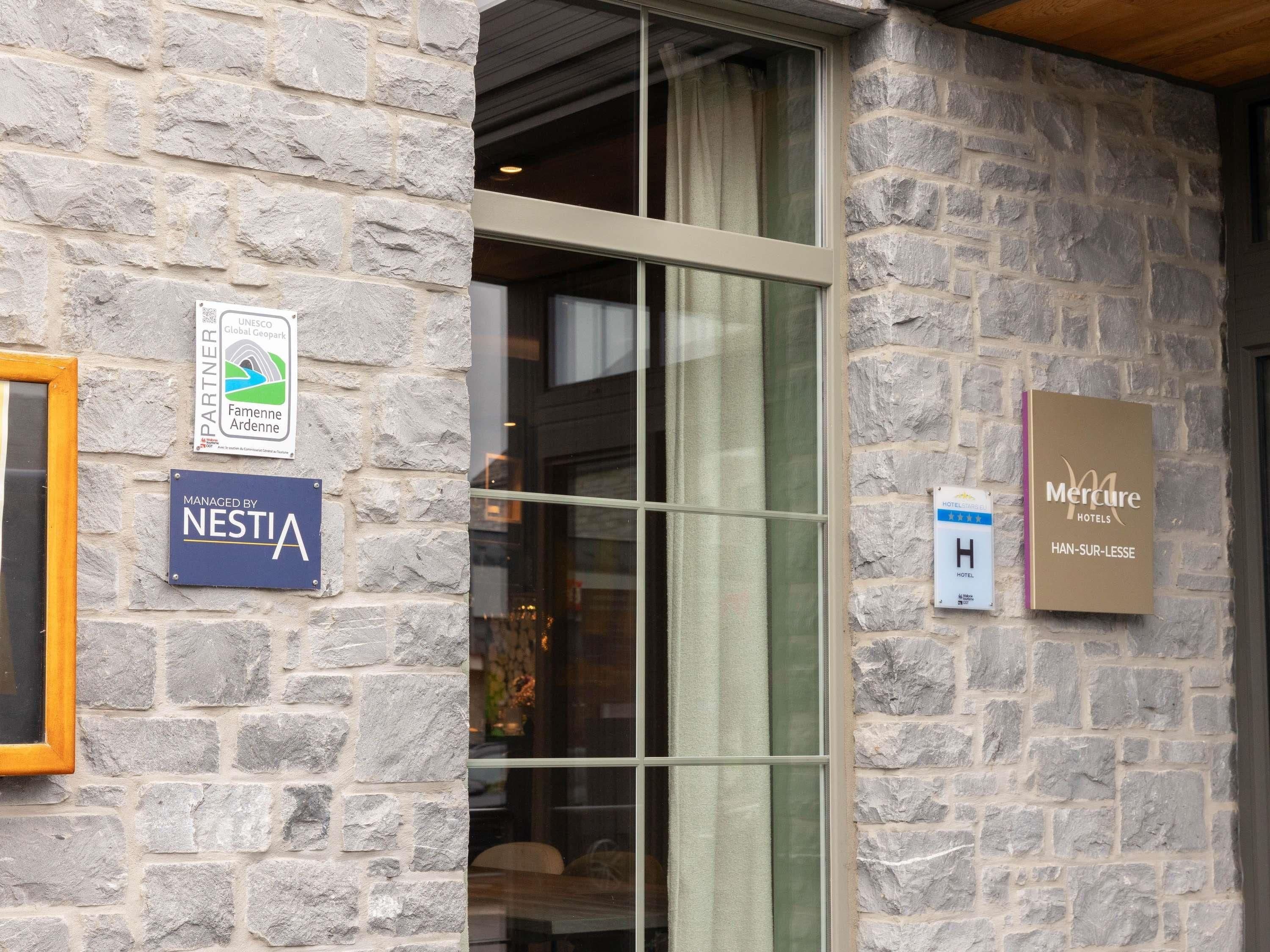 A stone building entrance with a glass door, signs for 'Nestia' and 'Mercure Hotels', and a 'Partner' sign.