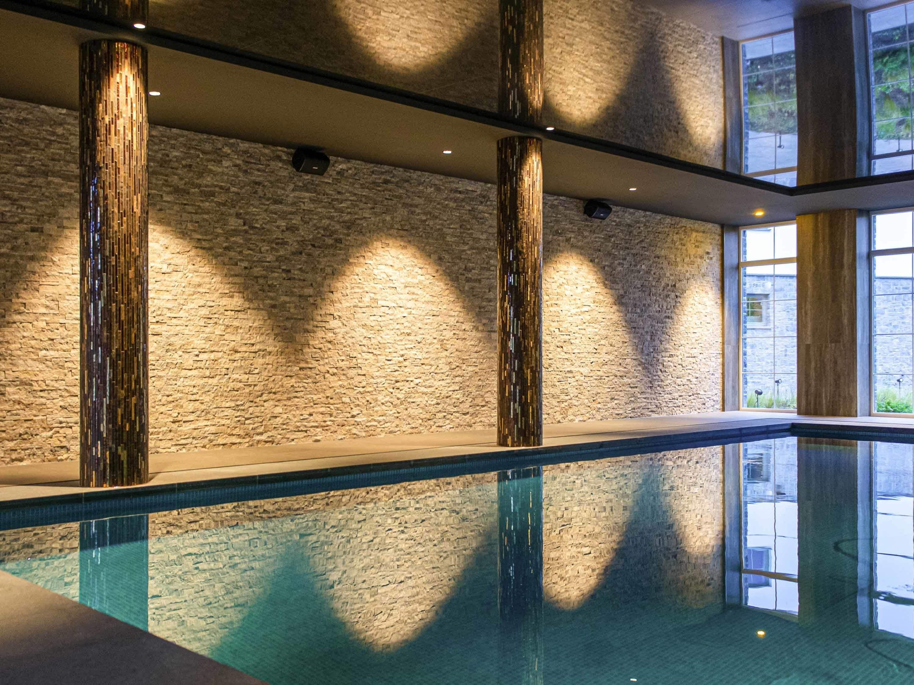 Piscina interior moderna com parede de pedra e colunas de madeira vertical.