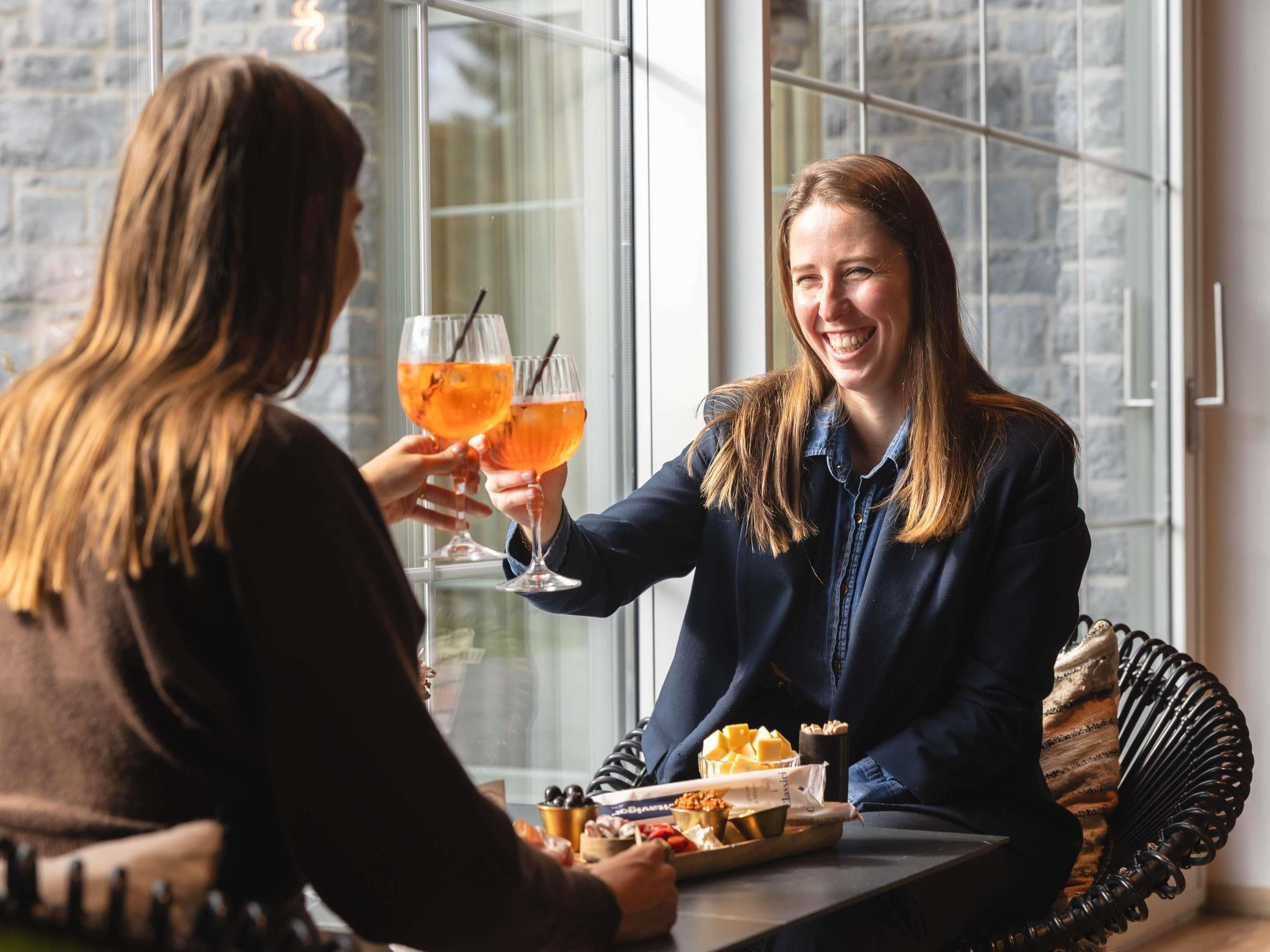 Dos personas brindando con bebidas en una mesa con comida y un vaso de bebida de naranja.