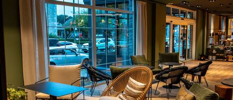 A modern interior with seating arrangements, a coffee table, and a view of the street through large windows.