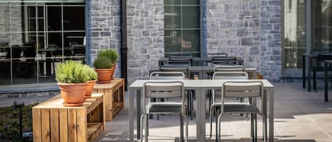 An outdoor dining area with stone walls, wooden benches, and metal chairs.