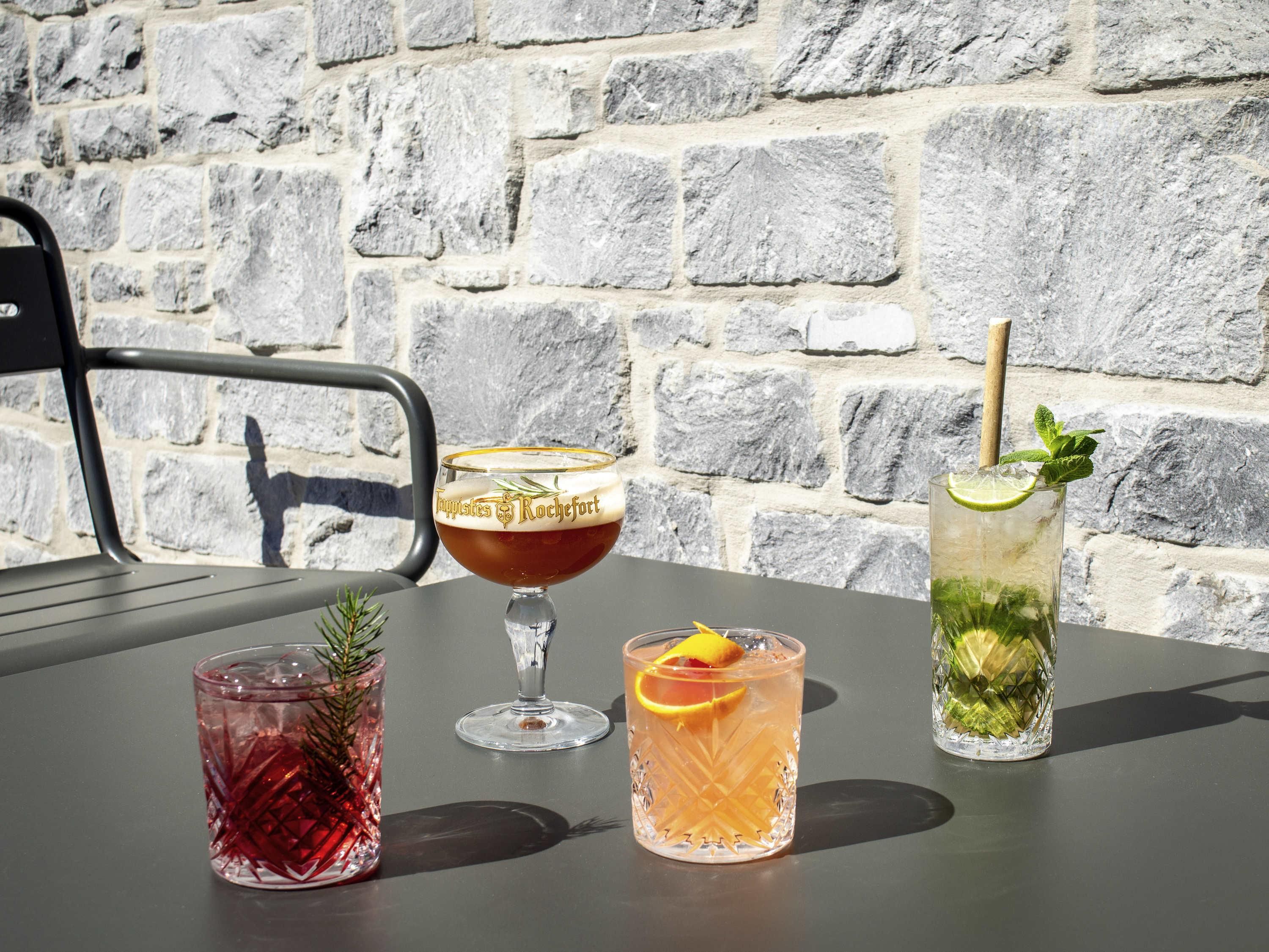 A table with four glasses of beverages, a chair, and a stone wall background.