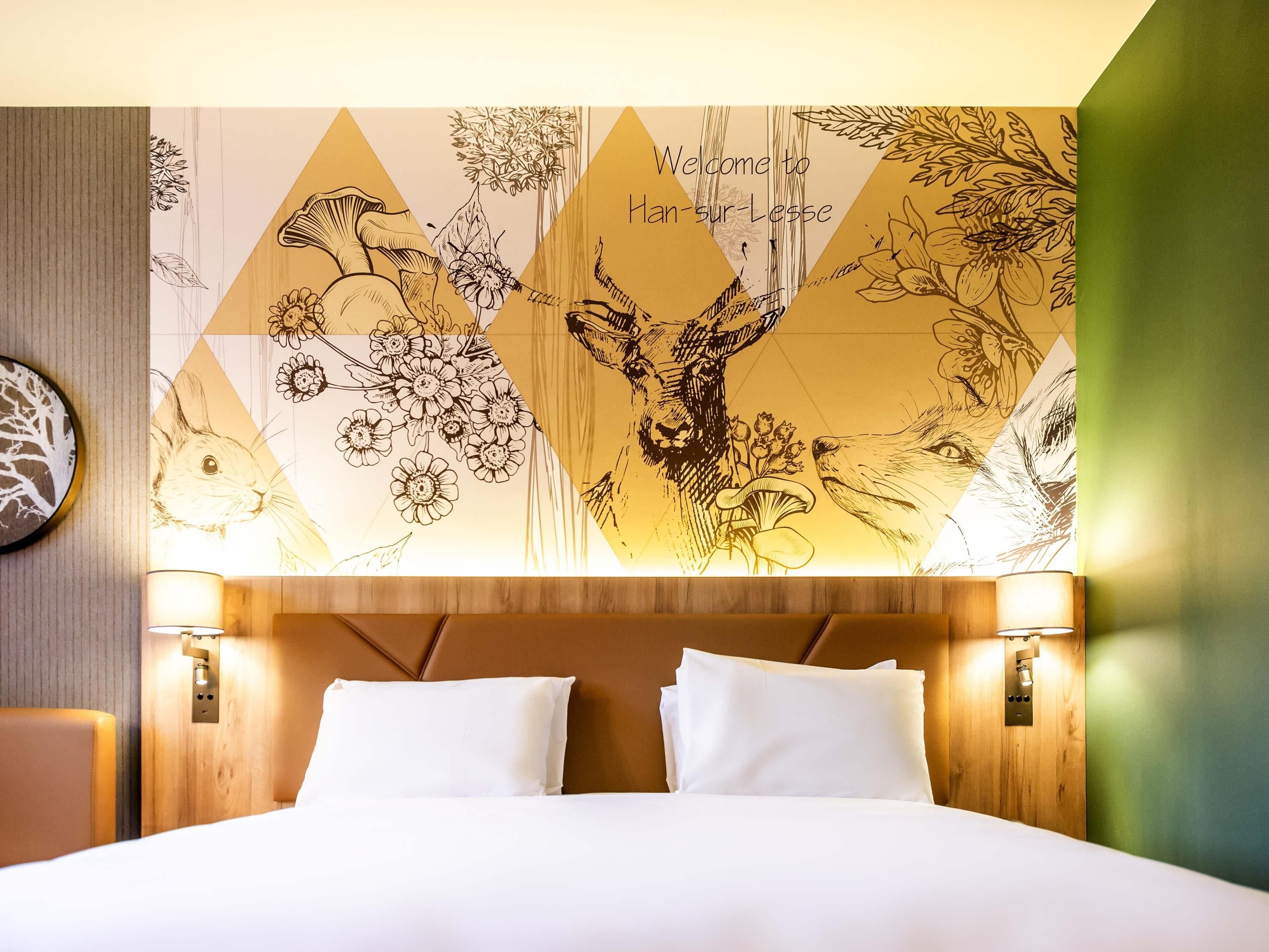 A hotel room with a bed, two bedside lamps, and a wall with a geometric floral and animal design.