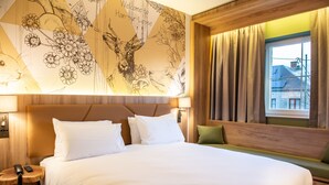 Une chambre d’hôtel avec un grand lit, une tête de lit en bois, un banc vert et une fresque murale.