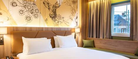 Una habitación de hotel con una cama grande, cabecero de madera, un banco verde y un mural en la pared.
