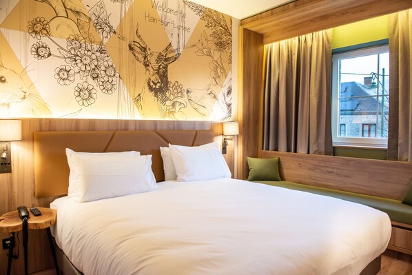 A hotel room with a large bed, a wooden headboard, a green bench, and a wall mural. - Mercure Han-sur-Lesse (Rochefort)