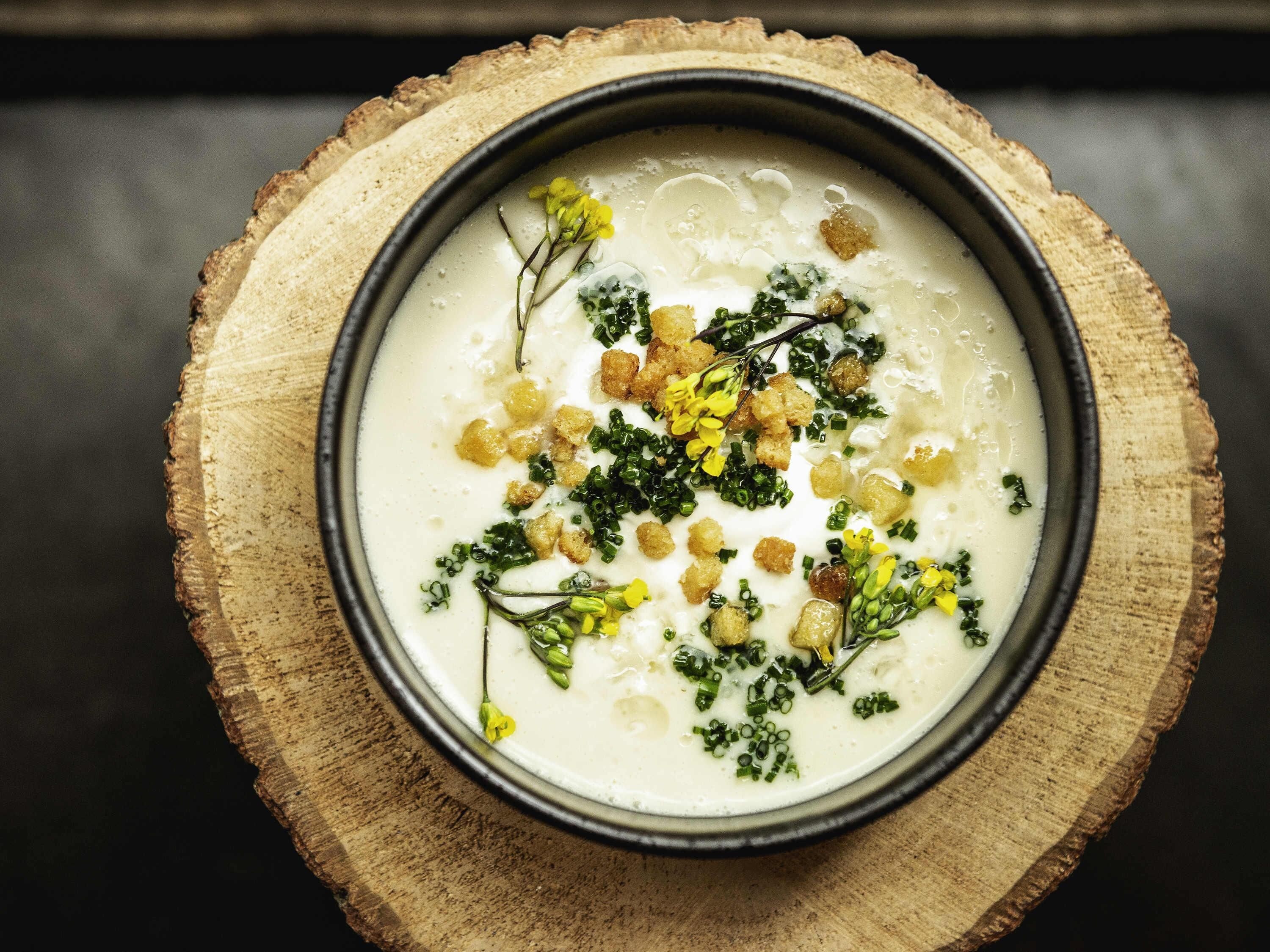 Uma tigela de sopa sobre uma tábua de madeira.