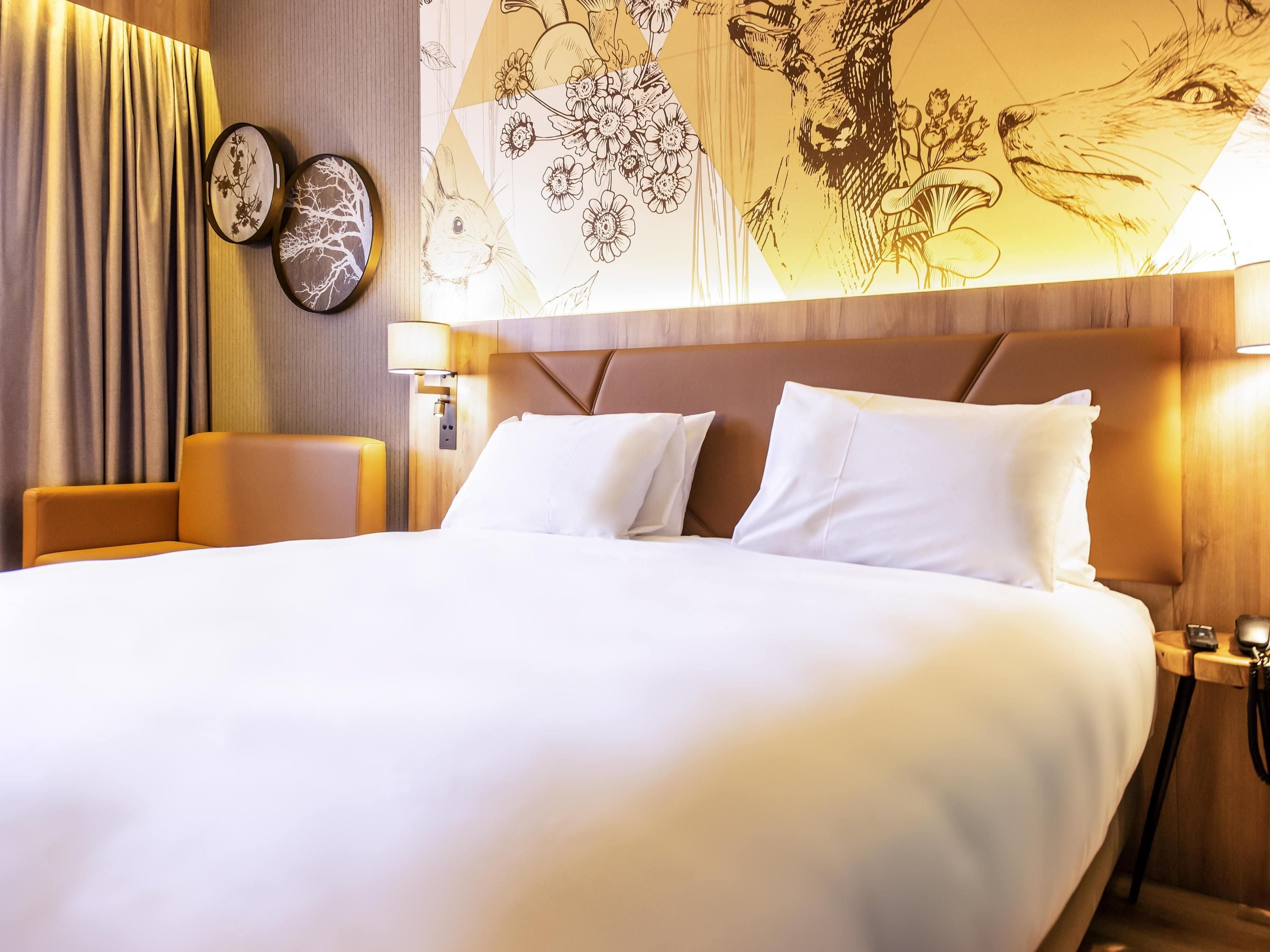 A hotel room with a large bed, a wooden headboard, and a wall with floral and animal illustrations.
